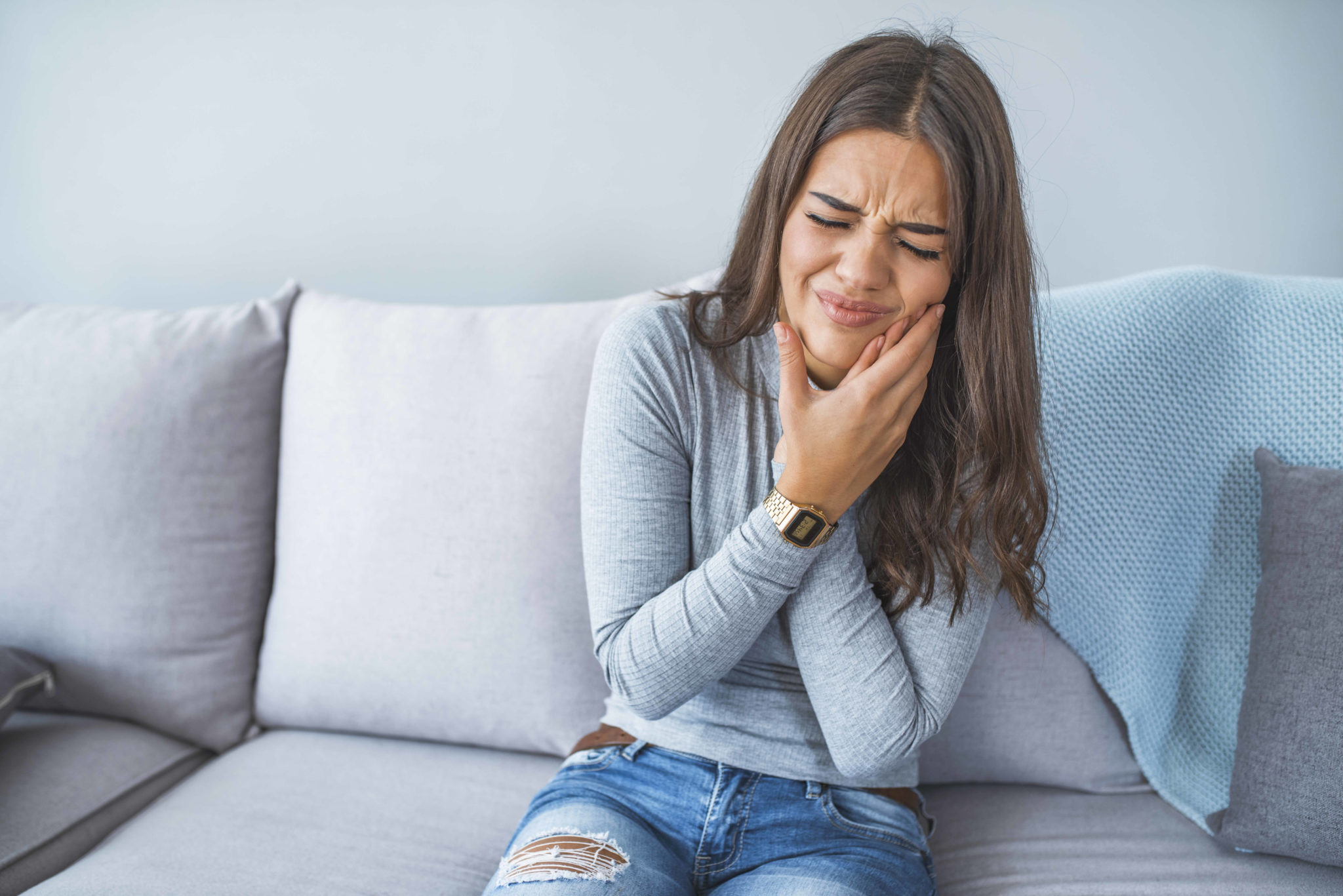 A woman holding her cheek in pain, in need of urgent dental care